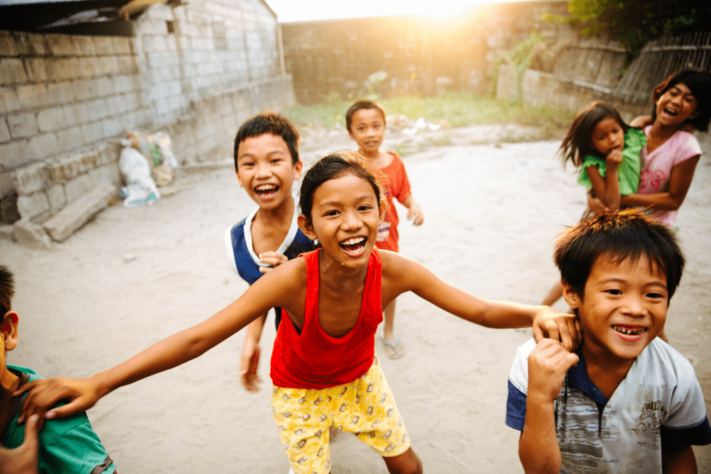 A group of children in the Philippines laugh and smile outside of a building
