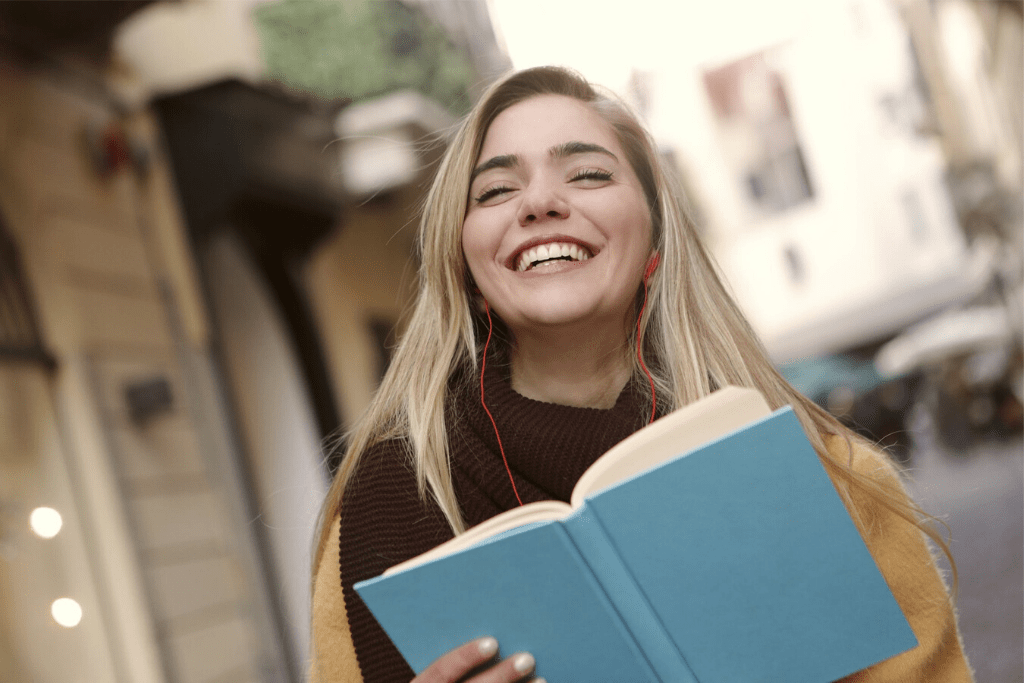 An English student smiles while reading a book outside