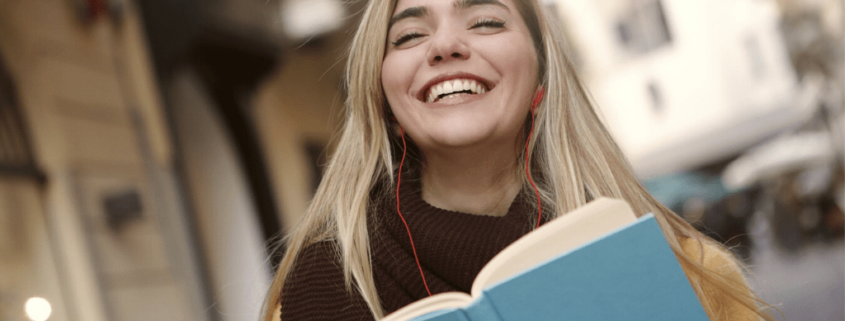 An English student smiles while reading a book outside