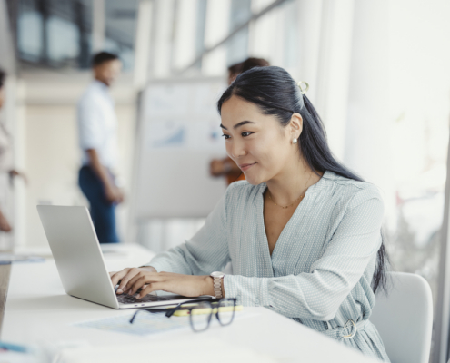 Business professional using a laptop in a collaborative office environment, representing workplace communication and productivity skills.