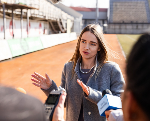 Sports organization representative speaking to reporters with microphones at a stadium during a media interview.