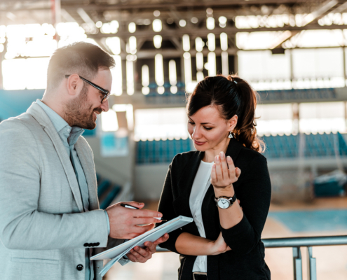 Sports management professionals reviewing documents in a stadium while discussing sports operations or event planning.