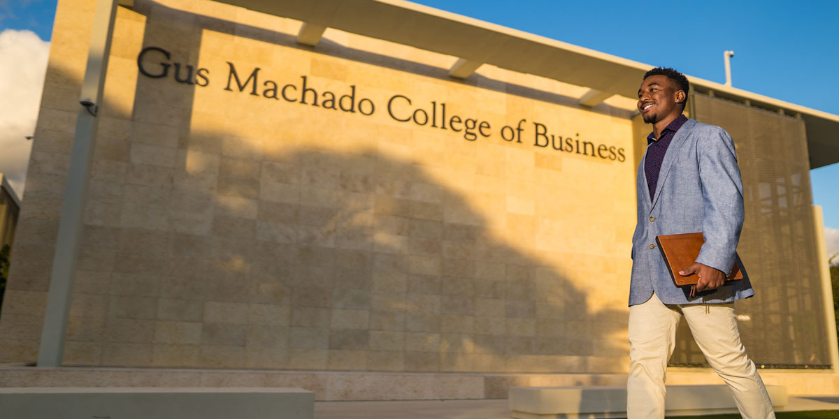 A young man walking in front of the Gus Machado College of Business